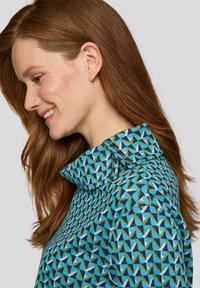 Kragenbekleidung mit geometrischem Muster in Blau, Grün und Weiß. Verfügt über eine strukturierte Oberfläche und eine Knopfverzierung am Kragen.