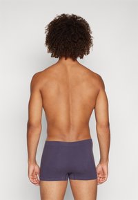 Dunkelviolette Boxer-Briefs mit glatter Textur, elastischem Bund und enger Passform, von hinten vor einem schlichten hellen Hintergrund betrachtet.
