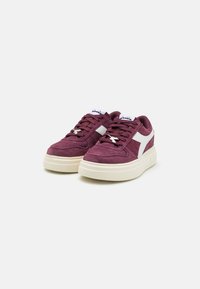 Sneaker in suède bordeaux con un accento in pelle bianca, punta rotonda e suola intermedia testurizzata. Presenta lacci piatti e un logo sulla linguetta.