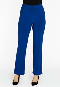 Blauwe stretchbroek met een elastische tailleband, recht toelopende pijpen, soepele textuur en een volledige lengte, gecombineerd met zwarte hoge hakken.