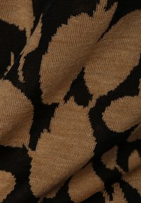 Tessuto a maglia con un motivo di stampa animale beige e nero. La texture è liscia, evidenziando il contrasto tra i colori e le forme.