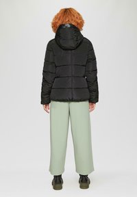 Schwarze gepolsterte Jacke mit Kapuze, mit horizontaler Steppung, glatter Textur und elastischen Bündchen. Kombination mit hellgrünen, weiten Hosen.