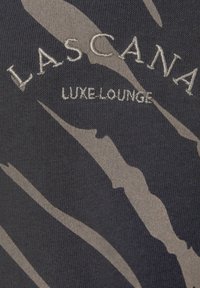 Maglia da loungewear in tessuto grigio scuro con strisce astratte grigio chiaro; presenta la scritta "LASCANA LUXE LOUNGE" ricamata con filo argento.