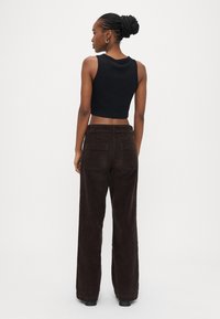 Top curto preto sem mangas combinado com calças largas de veludo cotelê castanhas, com bolsos traseiros e textura suave. Design e corte minimalistas.