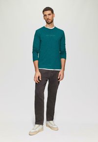 Błękitna koszula z długim rękawem i okrągłym dekoltem, z delikatnym wzorem strukturalnym. Połączona z ciemnoszarymi spodniami i jasnoszarymi trampkami.