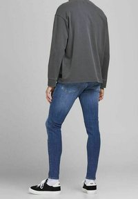 Camicia grigia a maniche lunghe, jeans blu slim-fit e sneakers nere. Design semplice con accenti minimi e una texture morbida.
