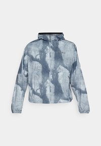 Blau-graue Jacke mit Kapuze, mit geometrischem Muster, durchgehendem Reißverschluss und elastischen Bündchen. Das Material sieht leicht und strukturiert aus.