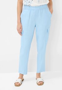 Light blue cargo pants with an elastic waistband, side pockets, and a relaxed fit. Flat woven texture. Worn with white slide sandals.