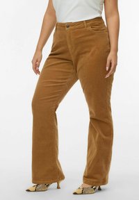 Pantaloni a zampa d'elefante in corduroy marrone con superficie texturizzata, tasche frontali e chiusura con bottone. Abbinati a scarpe con tacco a fantasia.