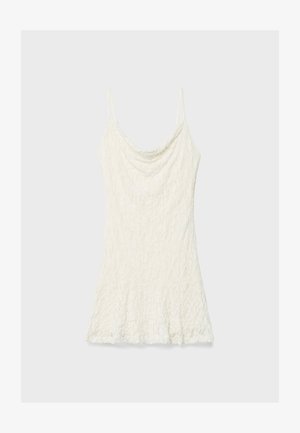White lace camisole with thin spaghetti straps, featuring a draped neckline and flared hemline. Textured fabric with a floral pattern.