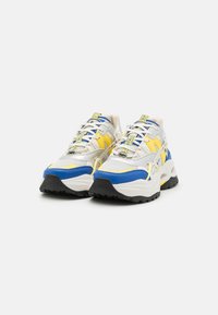Sneaker chunky bianche con accenti blu e gialli. Tomaia in rete e sintetico, suola in gomma nera spessa, sistema di allacciatura dettagliato, etichetta con logo.