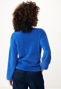 Klarblå, fluffig tröja med långa ärmar och rund halsringning, som visar en mjuk textur och en avslappnad passform. Matchas med mörka jeans.