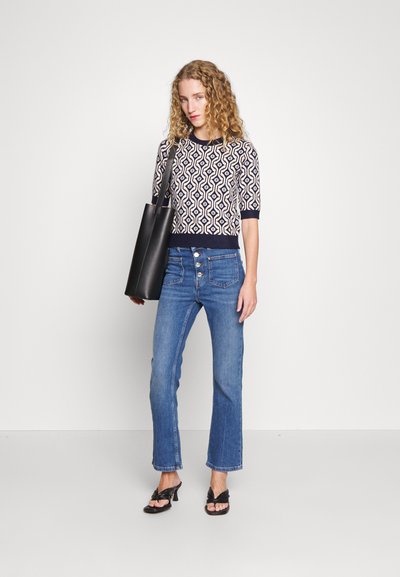 Knit sweater with geometric pattern in navy and cream, paired with high-waisted blue jeans, and a black tote bag. Simple black heeled sandals.