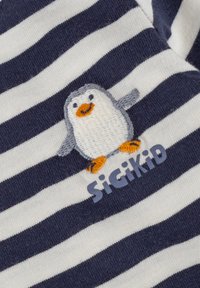 Navy- und weiß gestreifter Stoff mit einem gestickten Pinguin und dem Text "SiGiKiD" in Hellblau. Der Pinguin hat orangefarbene Akzente und einen lächelnden Gesichtsausdruck.