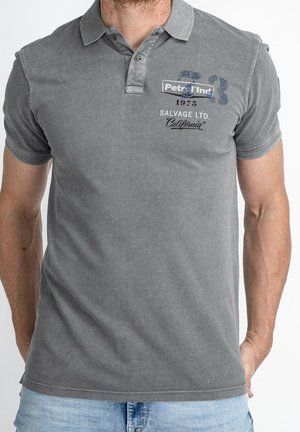 Grå polo med krave, korte ærmer og en slidt tekstur. Har branding foran og en dekorativ syningsdetalje.