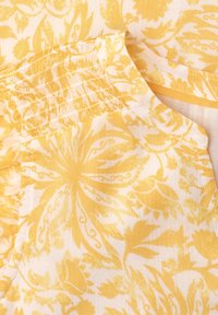 Tissu jaune à motif floral avec un empiècement froncé et un col rond.