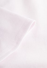 Hellrosa Baumwollstoff mit glatter Textur, einer umgeschlagenen Kante und sichtbaren Nähten. Keine Muster oder Hardwaredetails vorhanden.