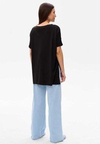 Czarna, oversize'owa koszulka z krótkimi, podwiniętymi rękawami i szczegółowym szwem z tyłu, w połączeniu z jasnoniebieskimi spodniami typu wide-leg. Gładka tekstura materiału.