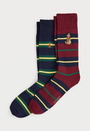Two pairs of striped crew socks, one navy with green and yellow stripes and orange polo player logo, one burgundy with navy, green, and yellow stripes and dog logo.