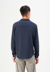 Navy lange mouwen shirt met een gestructureerd patroon, knoopmanchetten en een relaxte pasvorm. Achteraan is er een subtiele schoudernaad en een gebogen zoom te zien.