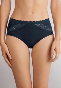 Hoge taille marineblauwe slipjes met bloemmotieven van kant langs de tailleband, een gladde stof en een aansluitend ontwerp.