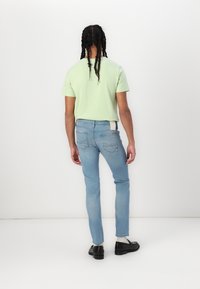 Camiseta de manga corta verde claro combinada con jeans ajustados de color azul claro. La vista trasera muestra costuras reforzadas y una franja en contraste en la cinturilla.