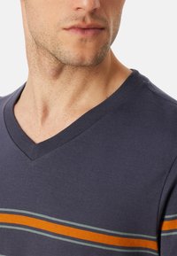 T-shirt z dekoltem w serek w granatowym kolorze z kontrastowymi poziomymi paskami w odcieniach pomarańczowym i zielonym. Prosty design z krótkimi rękawami i miękką fakturą.
