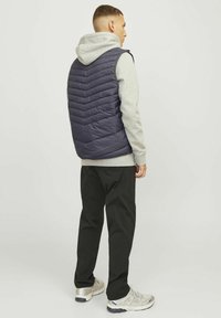 Marineblauwe gewatteerde puffer-vest met zigzagpatroon, gedragen over een grijze hoodie, gecombineerd met zwarte broek en zilveren sneakers.