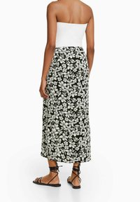 Květinová maxi sukně v černé barvě, se vzory bílých květin. Úzký pas se přechází do splývavého siluetu. V kombinaci s černými sandály na pásky.
