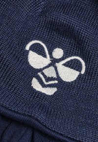 Marineblauer gestrickter Stoff mit einem strukturierten Muster, ausgestattet mit einem weißen bestickten Bienenlogo, das einen runden Kopf und verlängerte Flügel umfasst.