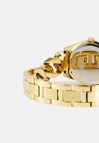 Orologio dorato con bracciale in metallo caratterizzato da maglie intrecciate. La cassa rotonda ha uno sfondo riflettente e una corona testurizzata.