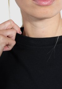 Zwarte katoenen t-shirt met een ronde hals. De stof lijkt glad met een lichte stretch. Een hand trekt aan de kraag.
