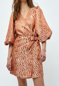 Kortärmad klänning i orange och beige med tigerstripemönster, med en omslagdesign och en knytning i midjan. Slät textur.