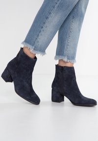 Navyblaue Wildleder-Stiefeletten mit Blockabsatz und seitlichem Reißverschluss. Vorgestellt zusammen mit hellblauen Jeans mit fransigem Saum.