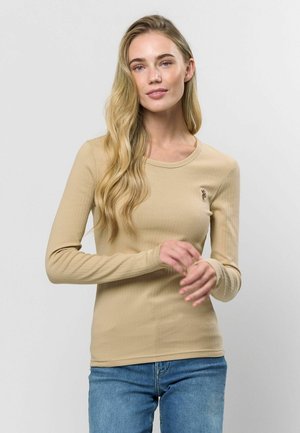 Kremlas garām piedurknēm ribota adījuma blūze ar apaļu dekoltē un mazu izšuvumu uz krūtīm. Saskaņota ar ziliem džinsiem.