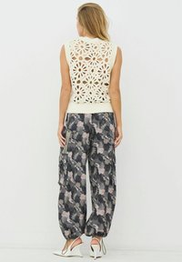 Krém színű kötött ujjatlan felső virágmintás csipkedíszítéssel, laza, terepmintás nadrággal szürke és rózsaszín árnyalatokban.