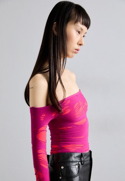 Pink off-shoulder top with a fitted design and large cut-out details. Paired with black pants featuring side pockets and a smooth texture.