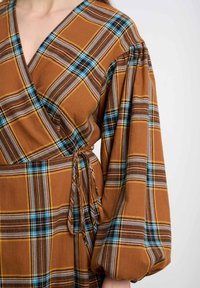Sukienka kopertowa w brązowo-żółtą kratę z niebieskimi akcentami. Charakteryzuje się efektownymi bufkami i wiązaniem w talii.