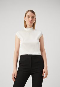 Hvit sateng uten ermer topp med høy hals, kombinert med svarte skreddersydde bukser, med en glatt tekstur og minimalt design.