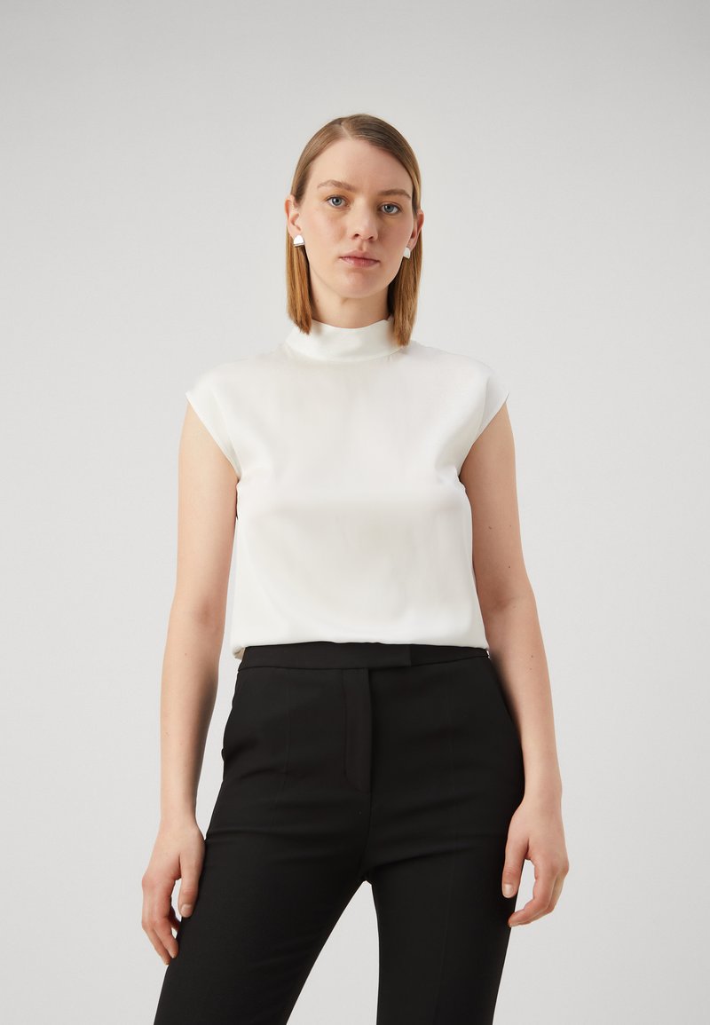 Hvit sateng uten ermer topp med høy hals, kombinert med svarte skreddersydde bukser, med en glatt tekstur og minimalt design.