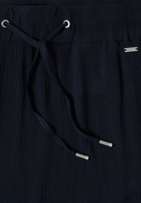 Tissu bleu marine avec des lignes verticales texturées, doté d'un cordon avec des embouts métalliques argentés et d'une petite étiquette de marque métallique rectangulaire.