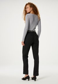 Grijze geribbelde lange mouwtop met een ronde hals, gecombineerd met hoge zwarte broek met streepjes. Zwarte hakken met details.