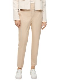 Pantalons beige ajustés fabriqués dans un tissu lisse, présentant une coupe slim et un longueur raccourcie, associés à des baskets blanches.