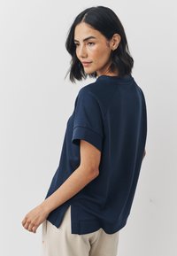 Navy blue casual top featuring short rolled sleeves, a rounded neckline, and side slits at the hem for ease of movement.