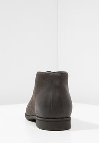 Bottine en daim marron foncé vue de dos, avec une couture centrale et une semelle en caoutchouc plate.