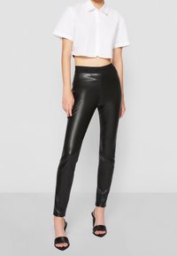 Svarta faux läderleggings med hög midja och en glänsande finish, i kombination med en kort vit skjorta med knappar och svarta klacksandaler.