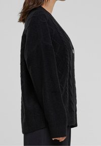 Cárdigan negro de punto trenzado con mangas largas, tejido texturizado, un escote en V profundo y botones en el frontal, con puños y dobladillo acanalados.