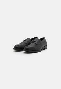 Svarte lærloafers med flat såle, med en glatt finish, en sydd detalj over vampsen og et diskret design.