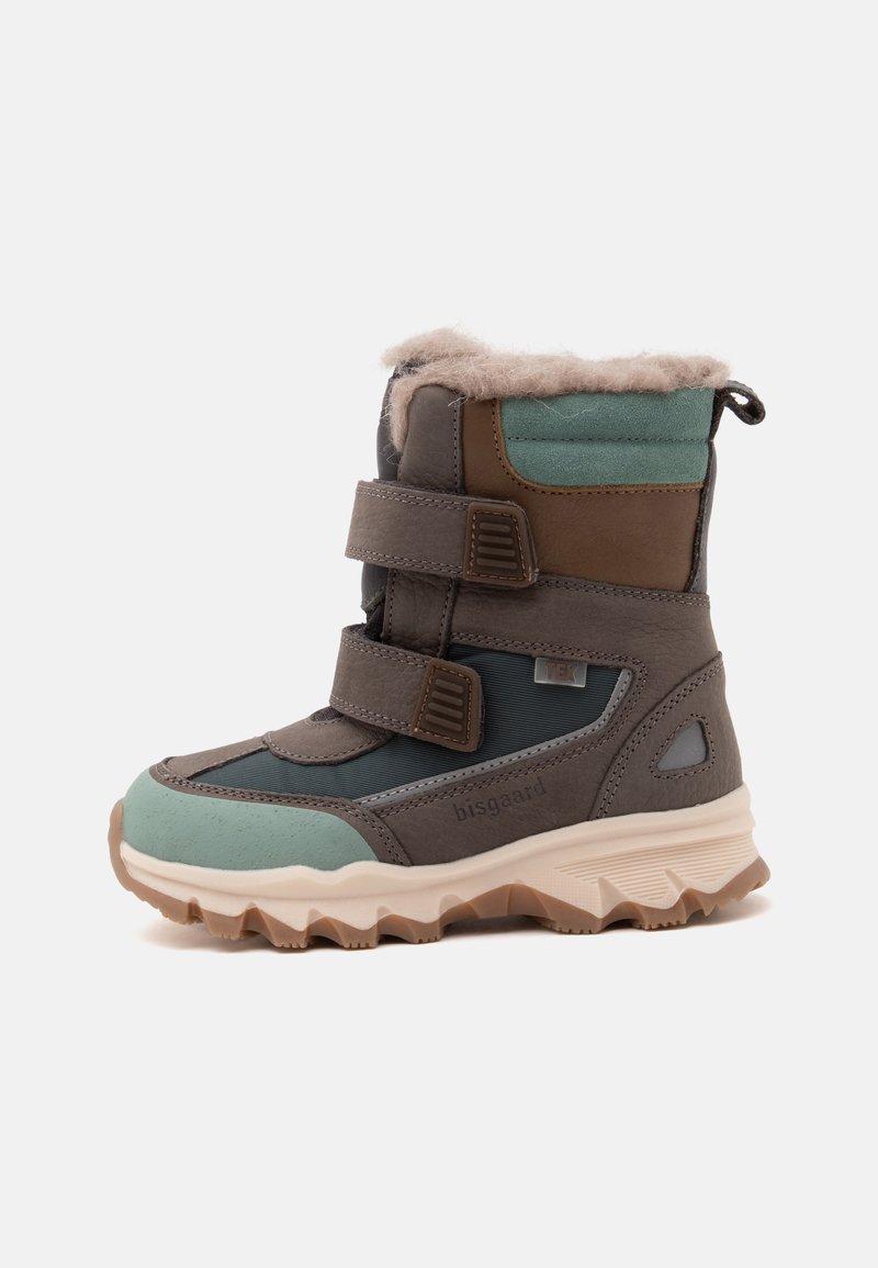 Botte d’hiver enfant avec panneaux verts et bruns, deux bandes velcro, semelle épaisse beige et doublure en fourrure beige douce autour du haut.