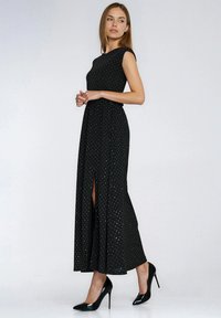 Czarna długa sukienka maxi z dopasowaną górą, krótkimi rękawami typu cap i srebrnymi groszkami. Posiada przedni rozcięcie i sięga aż do podłogi. Zestawiona z czarnymi szpilkami.